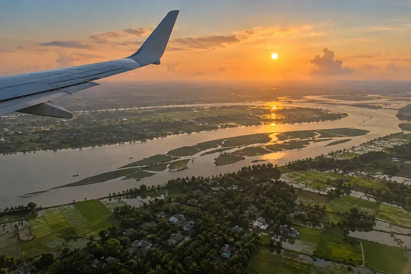 View from an aircraft window of the wing over a green river delta at sunset